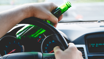 A person holding a beer bottle while driving a car
